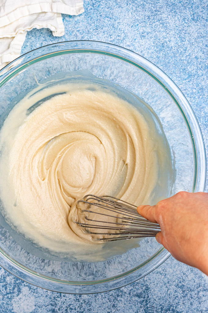 Coconut cream, and honey being whisked together in a large mixing bowl.