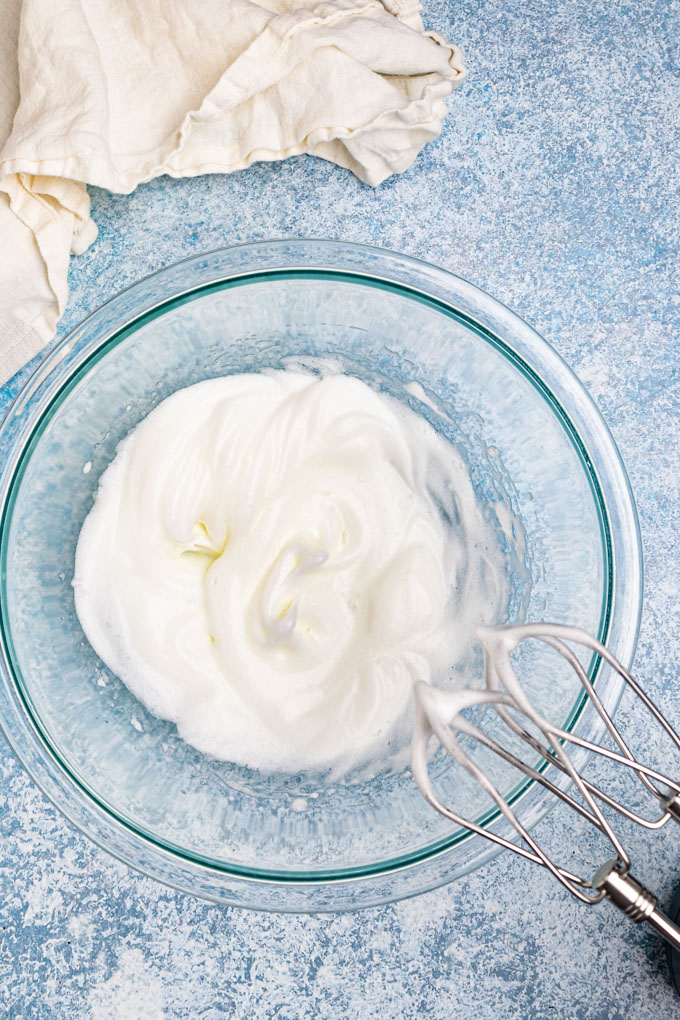 Egg whites in a bowl whisked up into stiff peeks with a hand mixer off to the side.