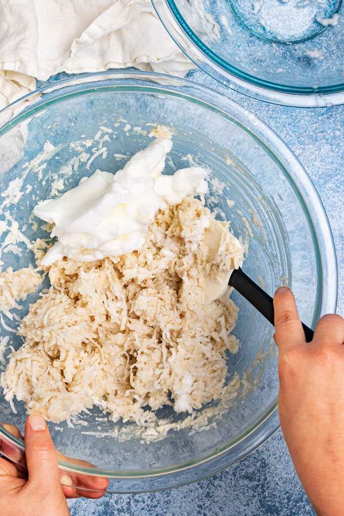 Hands stirring egg whites into macaroon batter.