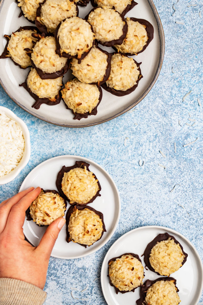 Coconut macaroons on a few plates on a light blue background, a hand is reaching for one of the cookies.