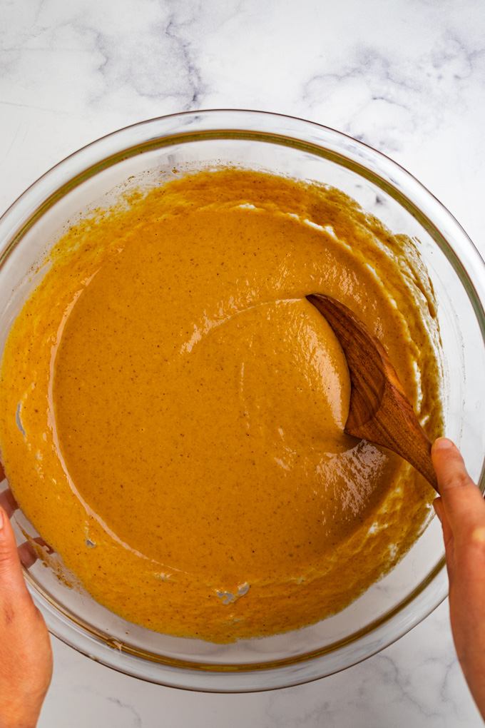 A glass mixing bowl with pumpkin pie filling. A wooden spoon is stirring the pumpkin filling.