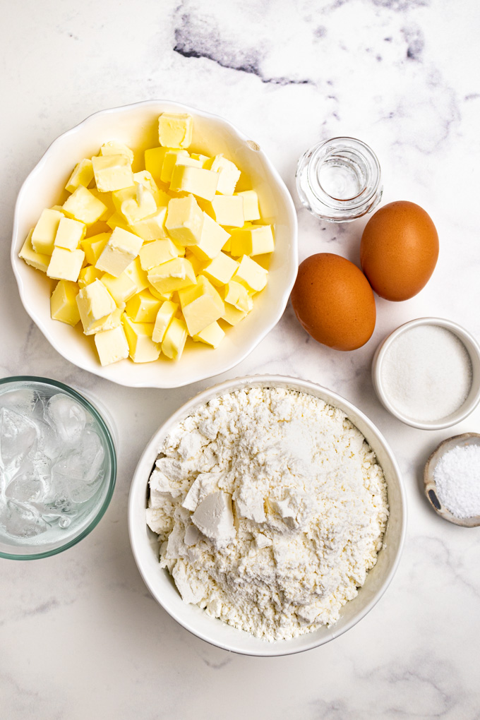 Ingredients for pie crust: cubed butter, eggs, ice water, flour, sugar, salt, and vinegar.