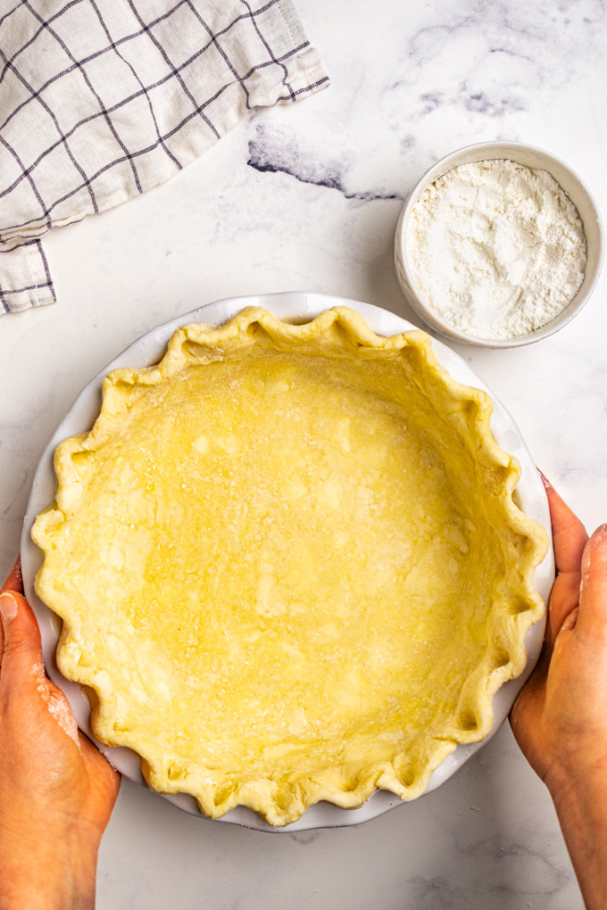 gluten free pie crust in a white pie plate, with crimped edges. Hands are holding the pie plate