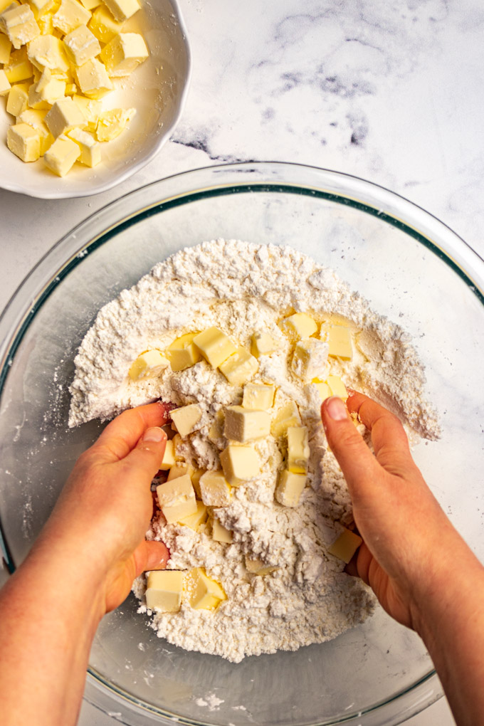 Cubes of butter being tossed in flour by hands, for making pie crust