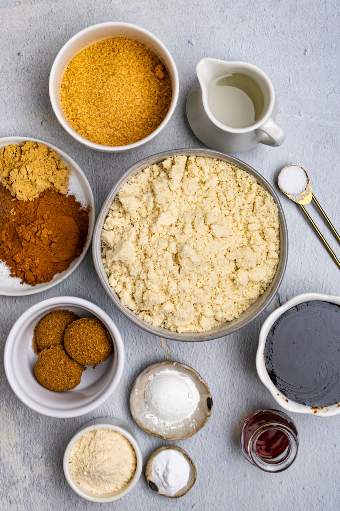 Ingredients for cookie in bowls: almond flour, spices, molasses, coconut oil, brown sugar, coconut flour, cornstarch, baking soda, vanilla, and salt