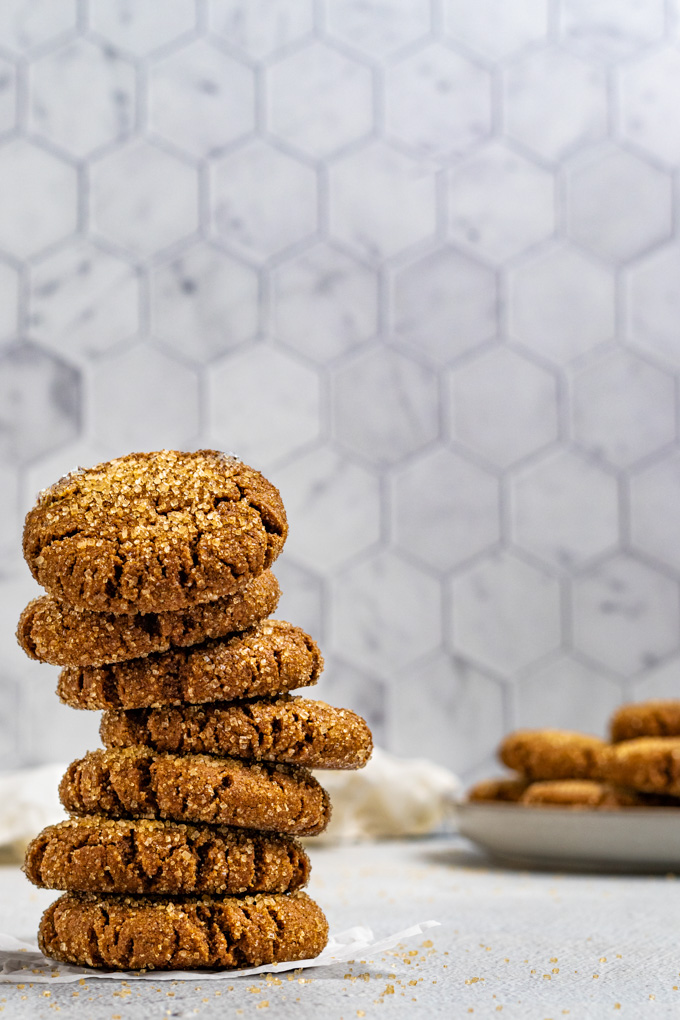 A stack of gluten free molasses cookies with a light gray background. A plate of the cookies are in the background.