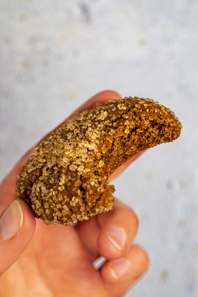 A close up of a gluten free molasses cookie with a bite taken out of it. A hand is holding the cookie upwards.