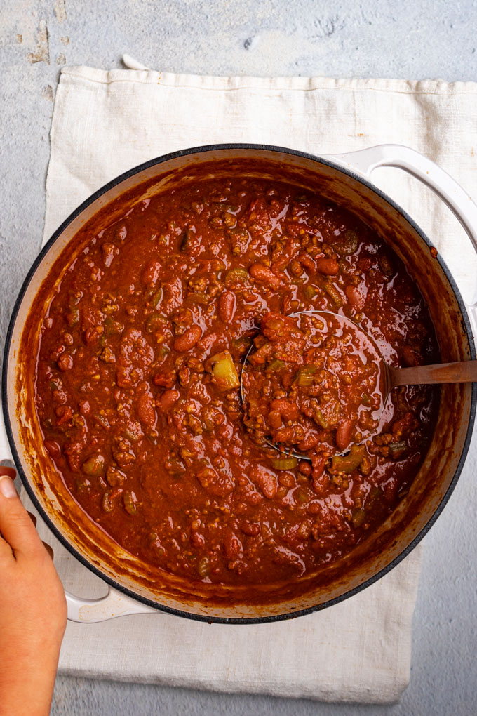Chili in a large ditch oven. A ladle is spooning out some of the chili.