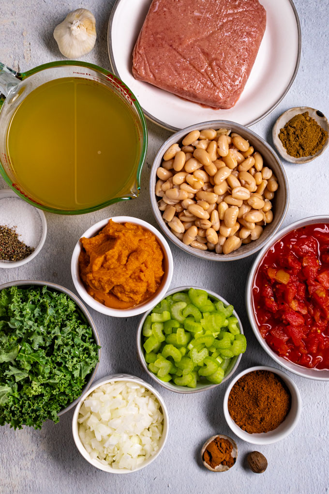 Overhead of photo of ingredients in bowls: ground turkey, chicken broth, white beans, pumpkin puree, canned, chopped tomatoes, celery, chopped kale, chopped onion, and spices.