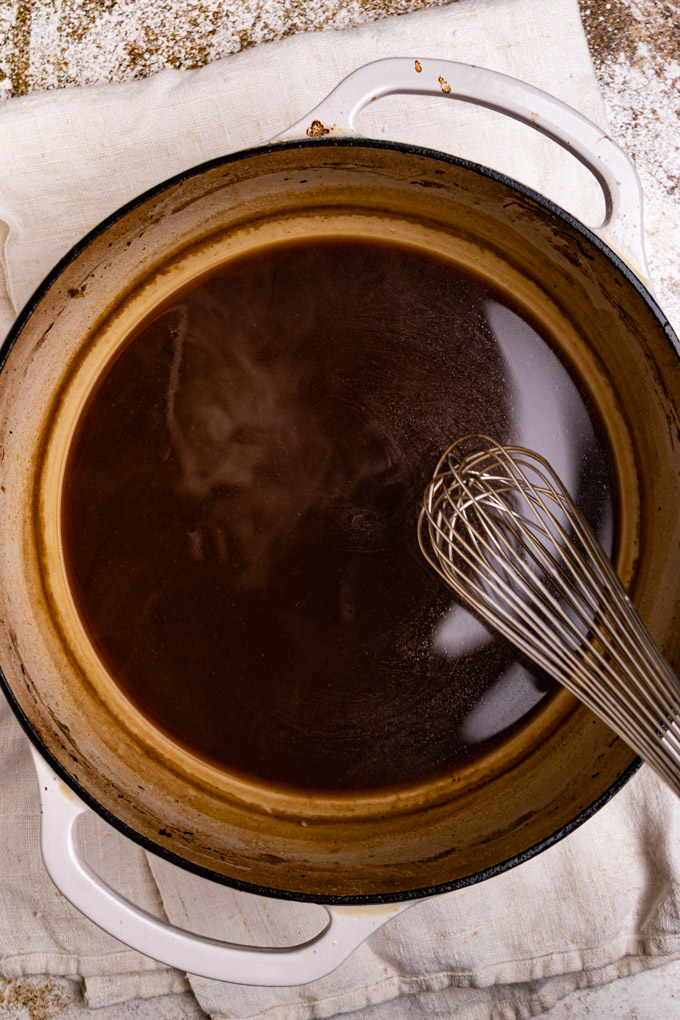 Gravy in a Dutch oven with a whisk being held over top of it about to stir it.