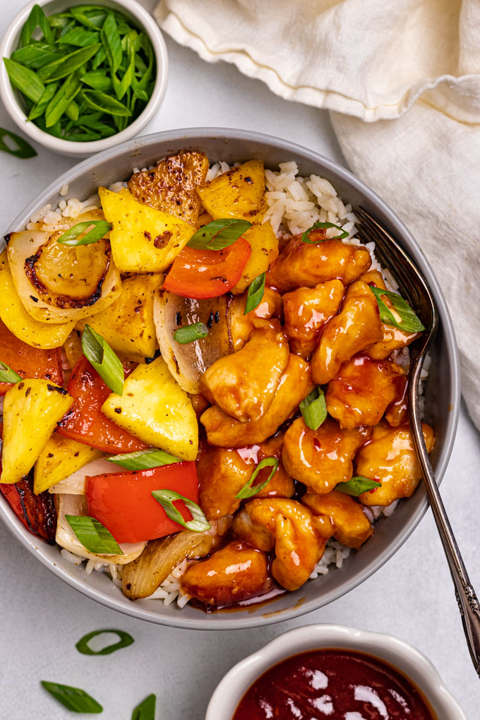 Sweet and sour chicken in a bowl over rice with a fork.