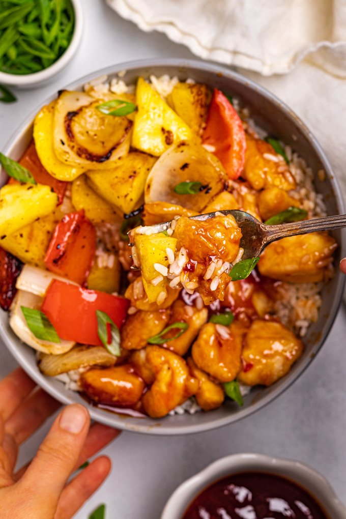 Sweet and sour chicken with pineapple in a bowl. A fork is holding ingredients up to the camera.