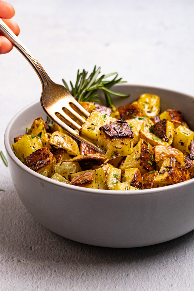 An angled shot of roasted potatoes in a bowl with a fork scooping some of the potatoes up.