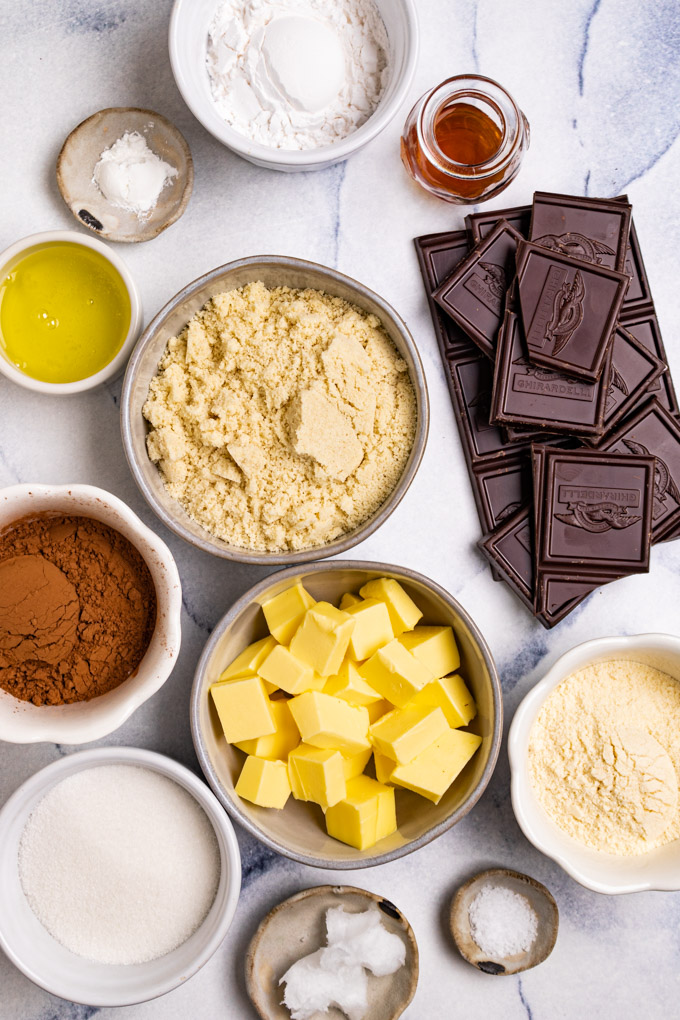 Ingredients in bowls: cubed butter, almond flour, sugar, cocoa powder, coconut flour, chocolate bars
