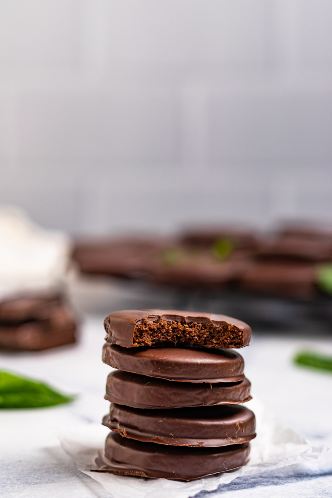 A stack of gluten free thin mint cookies with a bite taken out of the top cookie. There are more cookies blurred out in the background. 