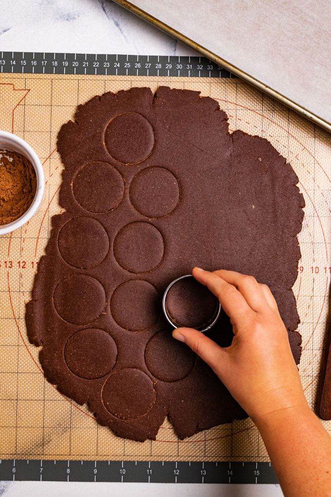 A hand is using a cookie cutter to cut out circles of gluten free thin mint cookie dough.