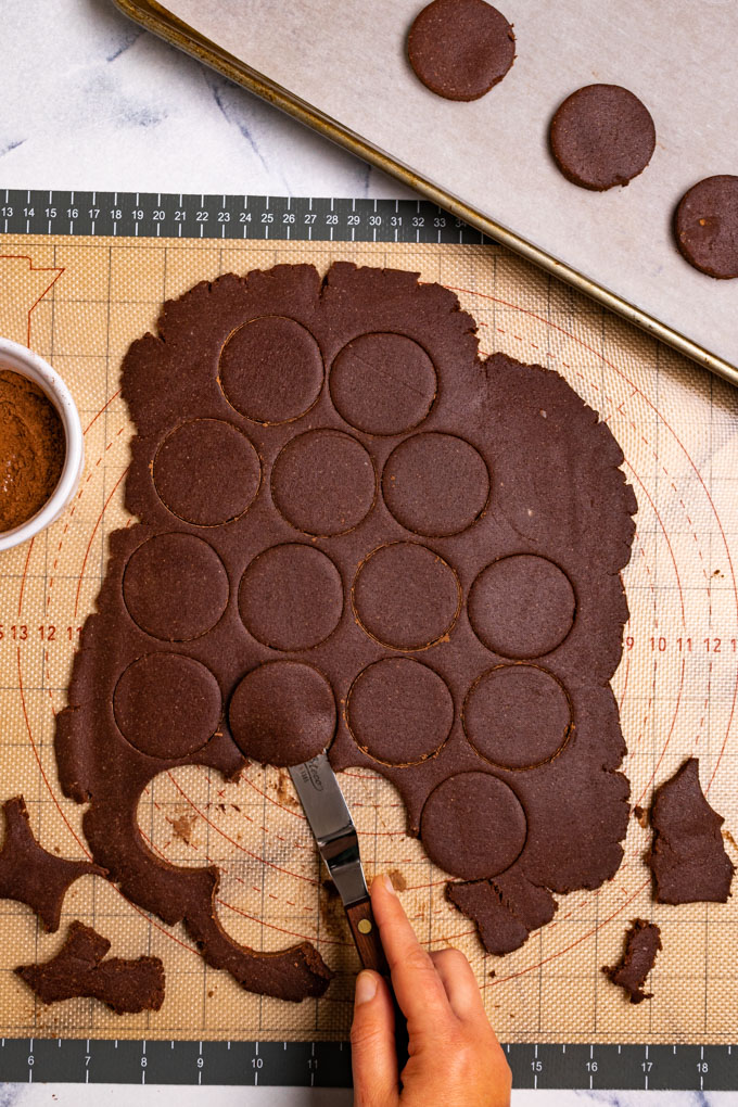 A hand is using an offset spatula to remove the circles of cookie dough that is cut into the thin mints cookie dough.