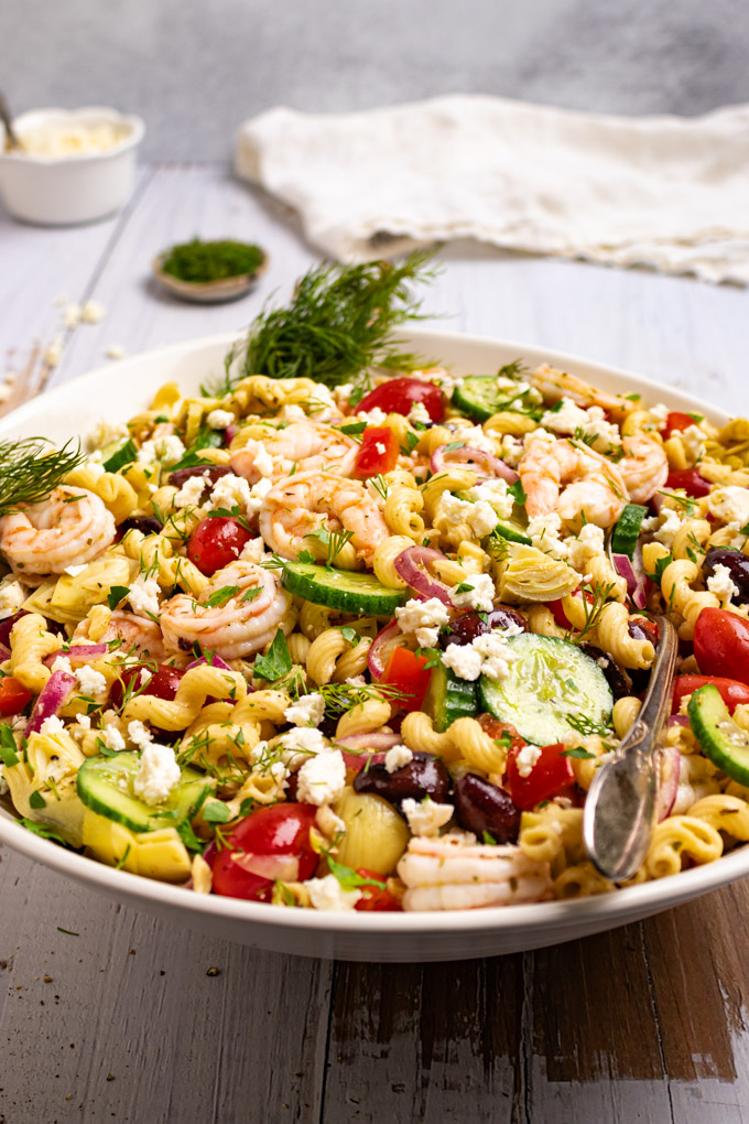 Angled shot of Greek Pasta salad in a large serving bowl on a rustic white wood background.