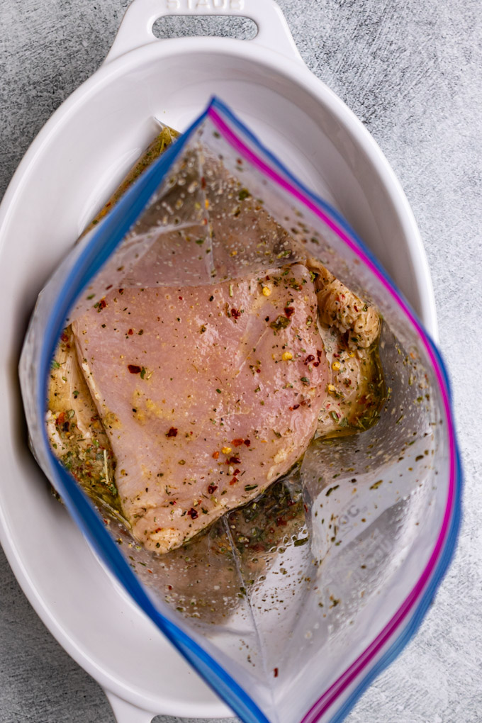 Overhead shot of raw chicken breast in an Italian marinade in a ziplock bag.