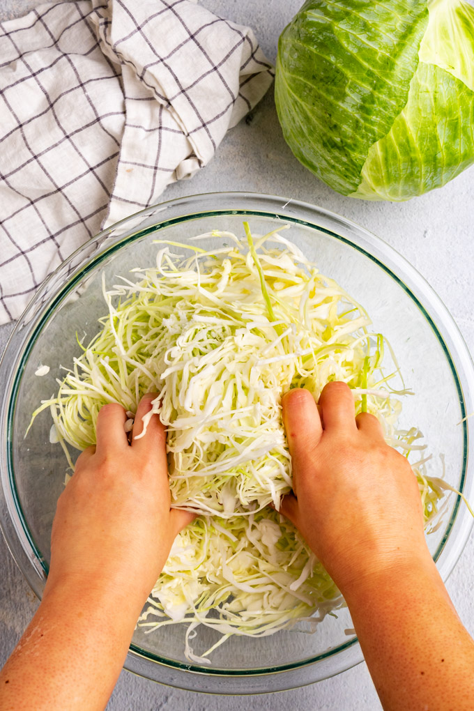 Hands massaging shredded cabbage for how to make sauerkraut.