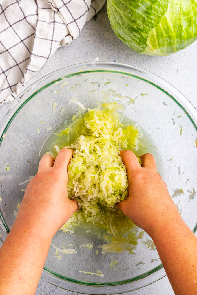 Shredded cabbage that has been massaged, and wilted down. Hands are massaging the cabbage to prepare it for sauerkraut.