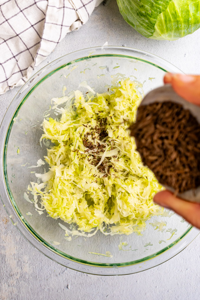 Caraway seeds are being added to a bowl of shredded cabbage that has been massaged, and prepared for sauerkraut.