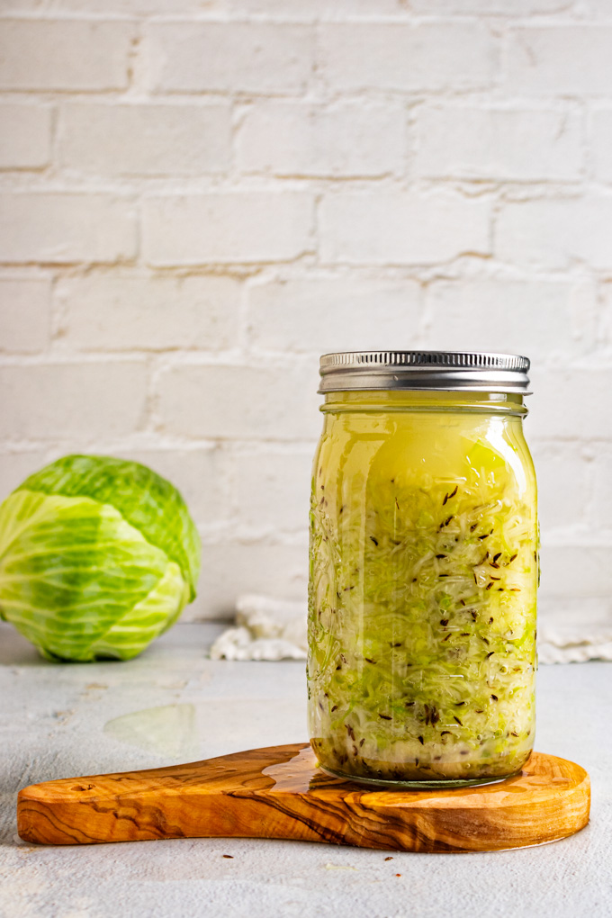 A straight on shot of shredded cabbage in a mason jar with a lid on. The cabbage is ready to be fermented into sauerkraut.