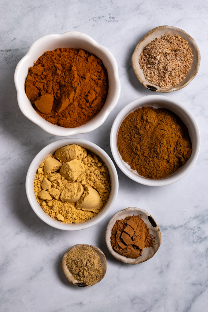 Ingredients in bowls: ground cinnamon, ground ginger, cloves, nutmeg, allspice, and caradamom.