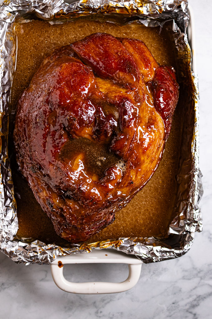 Overhead shot of cooked honey glazed ham in a baking dish, right out of the oven.
