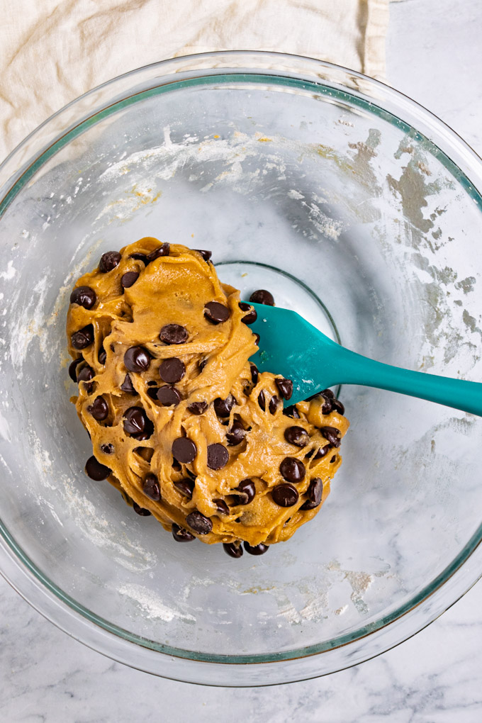 Chocolate chip cookie dough is mixed up in a mixing bowl with a spatula in the bowl.